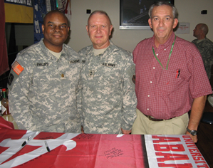 Army Maj. Darrell Phillips, a UA grad; Army Maj. Gen. Butch Pair, a Birmingham native and Crimson Tide fan; and Steven Hickam, a former UA ROTC instructor and current military contractor, stand by a UA flag signed by Crimson Tide fans and UA alums in Kuwait. The flag hung in a dining facility in Kuwait for four years, until soldiers decided a new one was needed because the old one was faded and in poor condition 