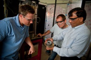 Agrawal, right, with graduate students Justin Williams, left, and Joseph Meadows examine the noise-reduction device made of a porous inert material of hafnium carbide and silicon carbide. 