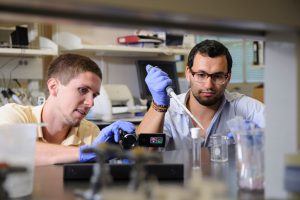 Hardaway, holding video camera, and graduate student Rami Ajjuri work inside a UA lab. 