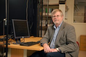 A professor sits at a computer desk.