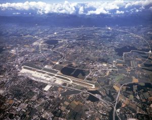 Aerial view of the CERN site just outside Geneva, with the Jura mountains in the background. The large circle shows the line of the LEP tunnel, 27 km in circumference, the small circle shows the SPS tunnel, 7 km in circumference. The crossed line indicates the the border between France and Switzerland (Image courtesy CERN). 