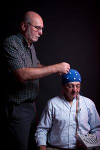Houser, standing, demonstrates how brain stimulation can be administered using a cap and electrodes in this photo illustration with Thoma, his UA colleague. 
