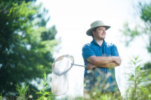 Lozier stands with two of his trusted tools, a good hat and a net for bee catching. 