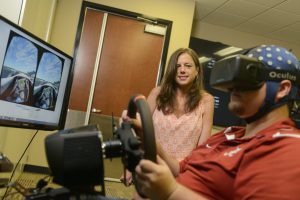 Miles Crabbe, a developer in UA's Center for Advanced Public Safety, sits in a replica of a race car cockpit and demonstrates a Virtual Reality research method while Erin O'Connor, a UA doctoral student in educational psychology, observes (Jeff Hanson). 