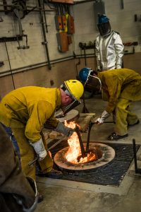 Craig Wedderspoon and others withdraw a pot of molten bronze from a furnace at UA's foundry. 