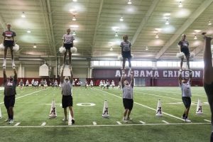 Male cheerleaders lift female cheerleaders into the air at cheer practice.