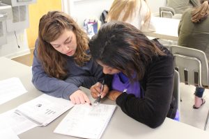 A student and a participant sit at a table while reviewing paper work. 