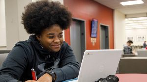 A students sits at a table and looks at a laptop computer. 