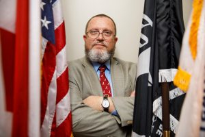 A professor studying veteran suicides stands amidst the U.S. and military flags.