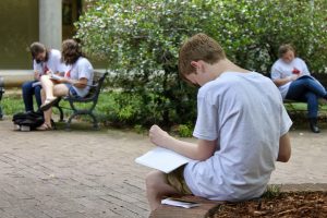 Young students sit outside reading and writing. 