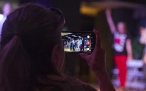 A woman uses a cell phone to film a theatre performance. 