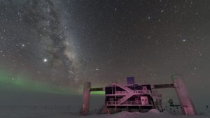 A science station, IceCube, sits in the white of Antarctica below a view of the night sky, with the Milky Way visible.