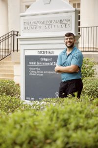 A male university student poses for a photo in front of an academic building