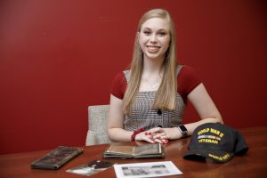 A female college student poses for a photo with her grandfather's Army mementos 