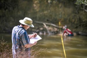 A biologist from The University of Alabama records data on the banks of a river.