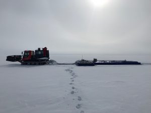 A PistenBully tows a flat radar on the baren, white ice of Greenland.