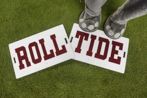 The feet and lower legs of UA mascot Big Al are shown stands near signs reading Roll Tide. 