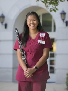 Arney poses for a picture while wearing nursing scrubs and holding a clarinet