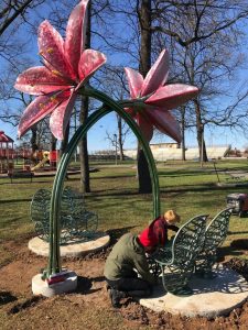 Workers install a pink flower structure at a park. 