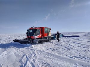 A red, tracked vehicle pulls a large, flat antenna across the white, Antarctic ice.