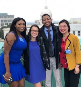 Four college students pose in front of city buildings in Montgomery