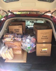 The trunk of a car is loaded with bags and boxes of food. 