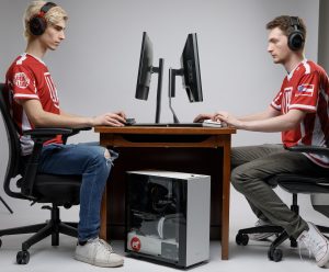 Two men sit facing each other playing video games on a computer.
