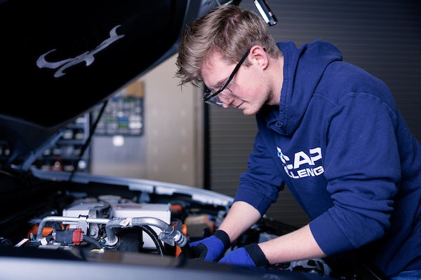 A student leans in to work under the hood of a car
