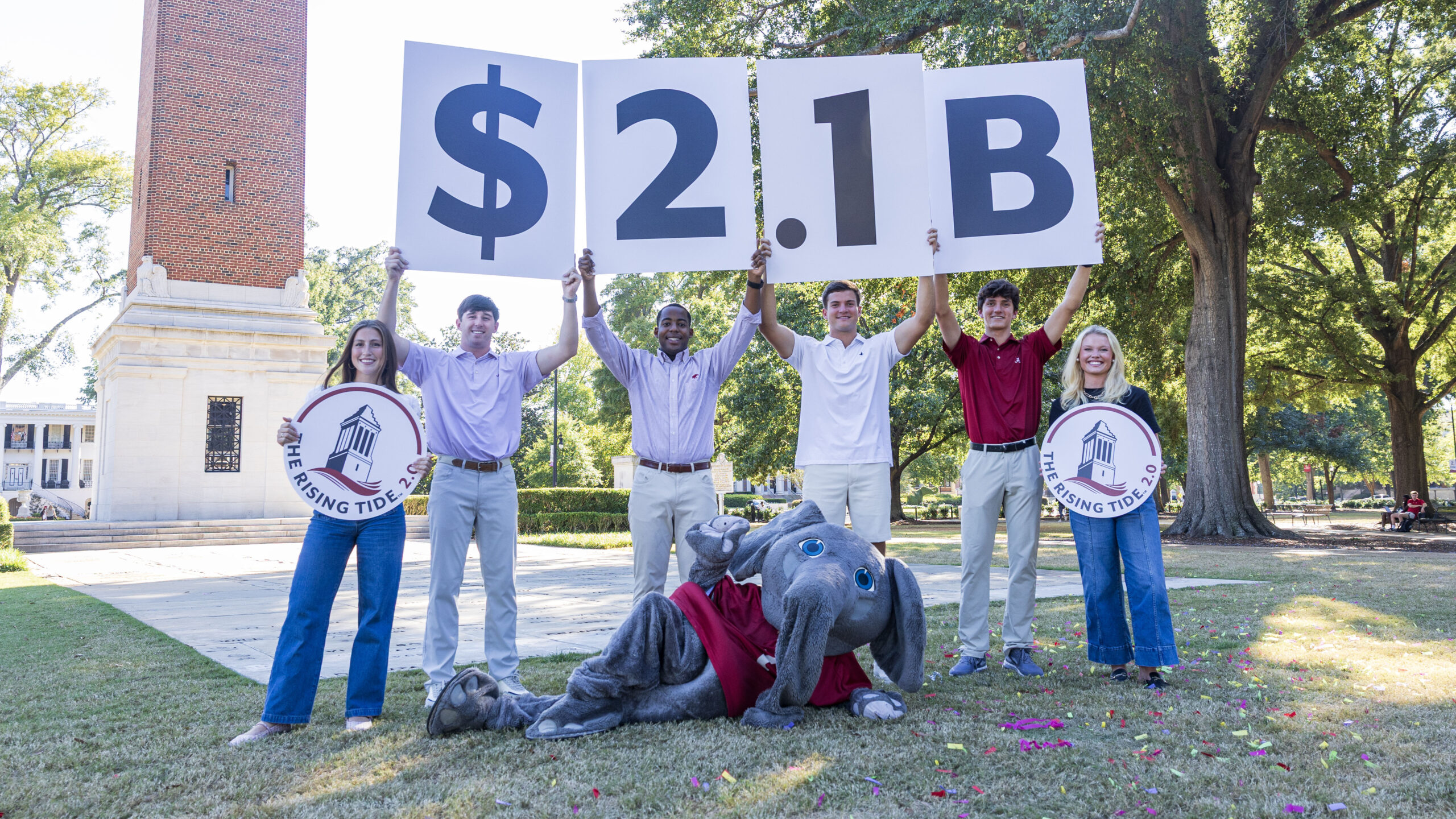 Male and female college students hold signs and pose for a photo with an costumed elephant