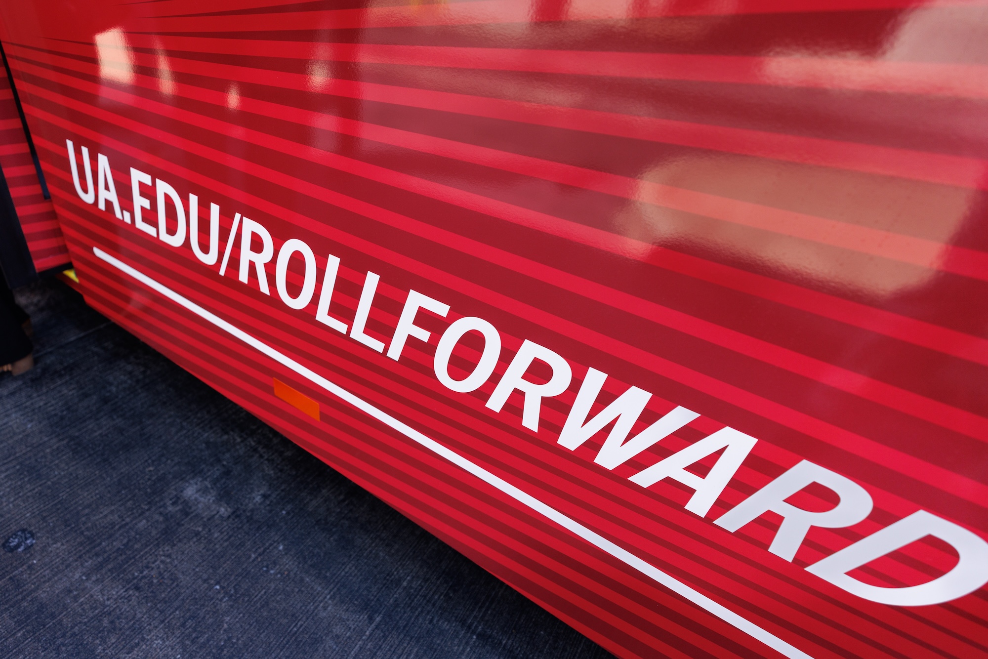 The web address ua.edu/rollforward on the striped red side panel of a bus.