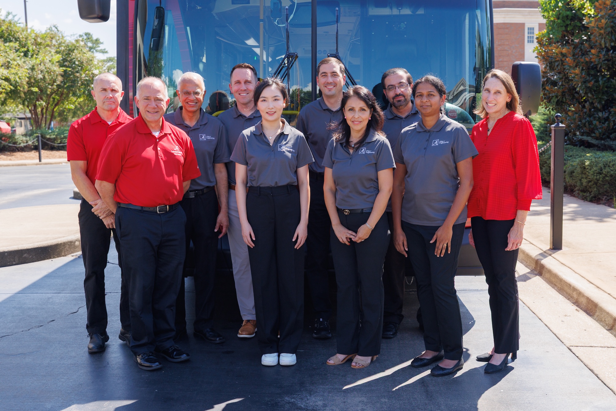 UA College of Engineering faculty, staff and transit partners stand in front of a red bus for a group portrait.